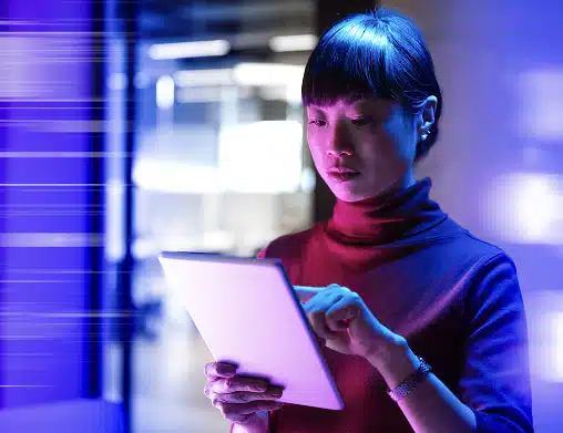 Female employee with short black hair focusing on her tablet in a server room