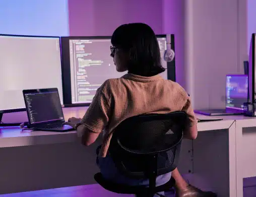Female employee in business casual clothes sitting at her desk coding