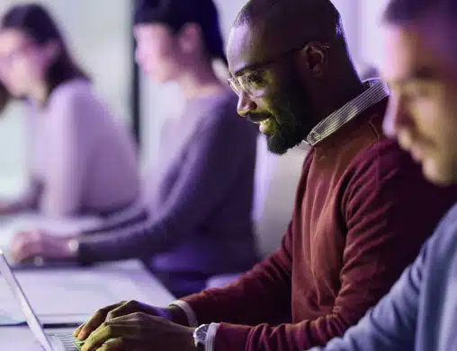 Group of diverse employees sitting at their workstations typing on their laptops and smiling